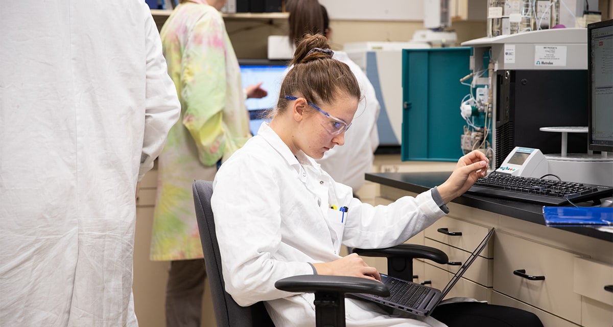 Student in labcoat looking at laptop